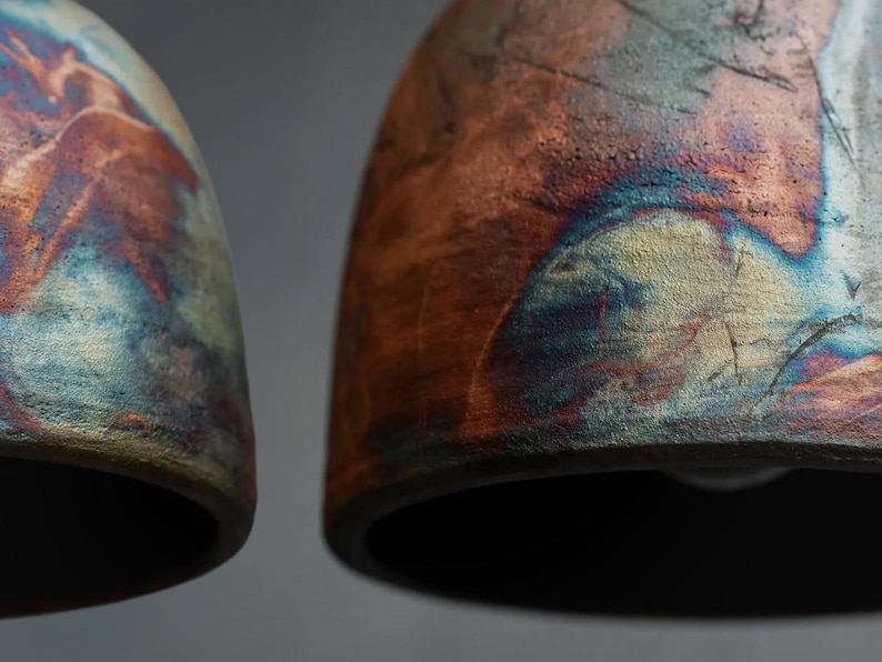 May include: Two dome-shaped ceramic pendant lights featuring a textured, multi-coloured glaze. The surface displays a blend of deep copper, burnt orange, and metallic blue tones with a rough, matte finish and visible cracks across the curved exterior.