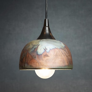 May include: A pendant light fixture with a ceramic shade. The shade has a brown, green, and blue mottled pattern. The fixture has a black metal top and a white bulb at the bottom. The light hangs from a black cord.