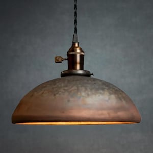 May include: A rustic, dome-shaped pendant light fixture with a distressed, metallic finish. The light is suspended from a black cord and has a simple, industrial design.