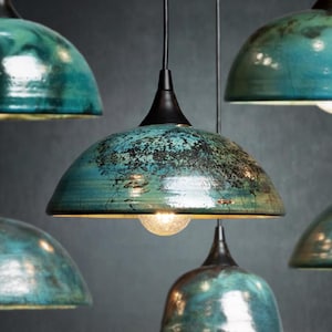 May include: Several teal and black pendant lights with a distressed finish hang from the ceiling. Each light has a dome-shaped shade and a black fixture. The lights are illuminated, casting a warm glow.
