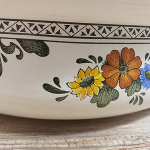 May include: White ceramic bowl with a floral design featuring yellow, orange, and blue flowers. The bowl has a black and white geometric border.