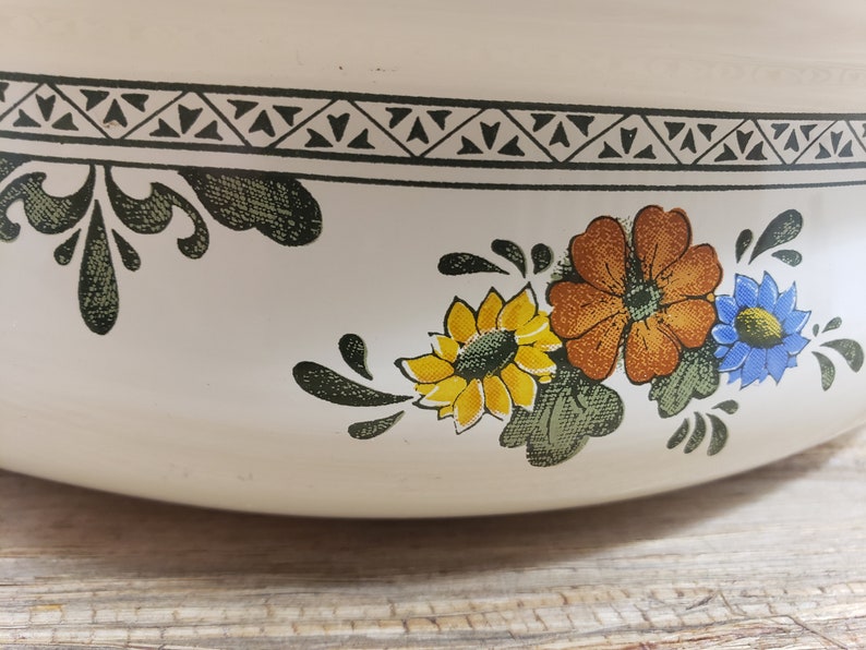 May include: White ceramic bowl with a floral design featuring yellow, orange, and blue flowers. The bowl has a black and white geometric border.