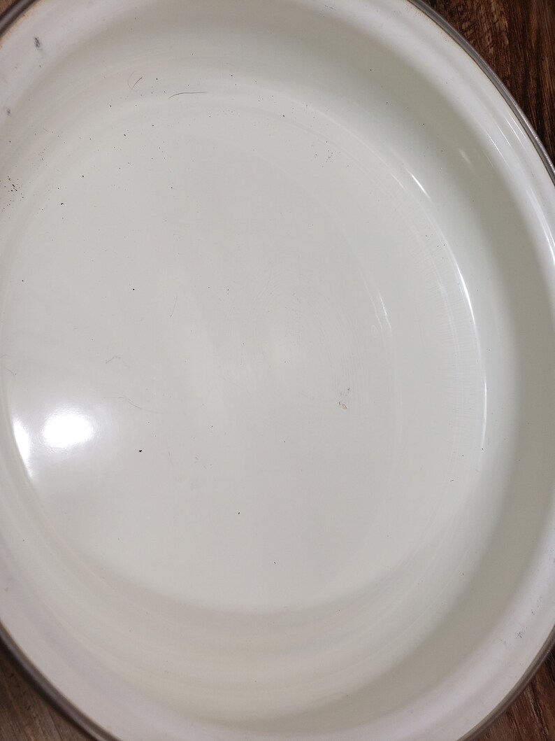 May include: White enamel baking dish with a slightly rounded rim. The dish is empty and clean.