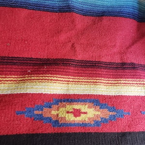 May include: A colorful woven blanket with a red, blue, yellow, and white striped pattern. The blanket has a geometric design in the bottom right corner.