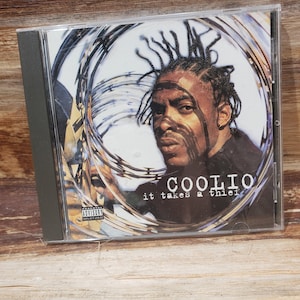 May include: A CD case with a black and white photo of Coolio on the front. The background is a blurred image of barbed wire. The text "COOLIO it takes a thief" is printed in white on the front of the case. The case has a parental advisory sticker on the bottom left corner.