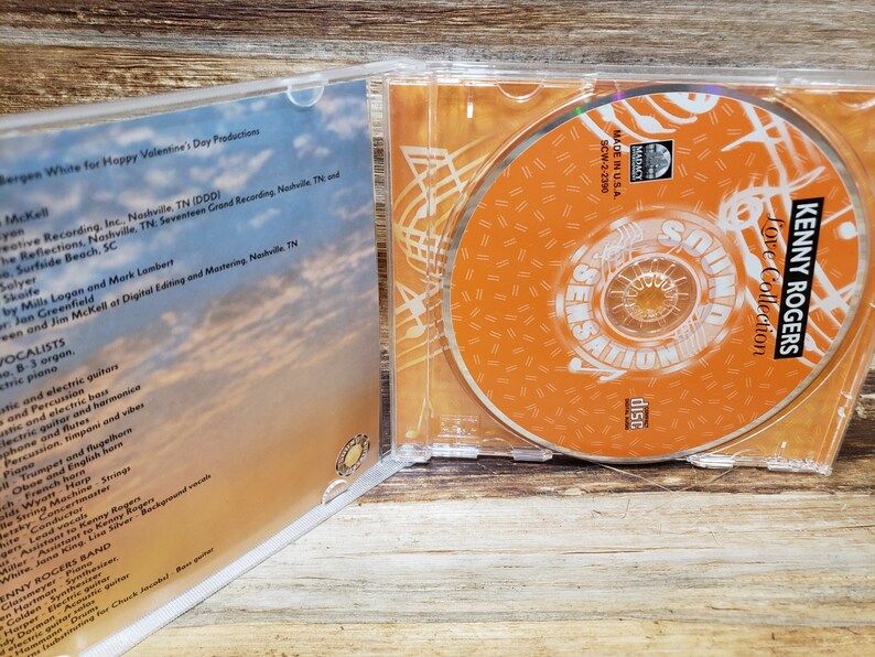 May include: A clear plastic CD case with a CD inside. The CD is orange with white text that reads "Kenny Rogers Love Collection". The case is open, revealing the CD and the album's liner notes.