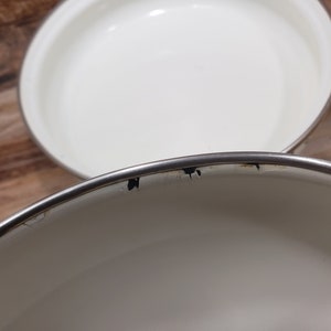 May include: Two white enamel cookware pots with silver rims. The top pot has a few black marks on the rim.