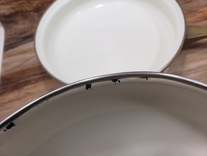 May include: Two white enamel cookware pots with silver rims. The top pot has a few black marks on the rim.