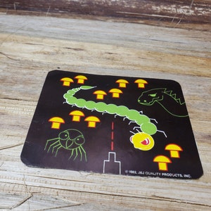May include: A vintage black game board featuring a green centipede, a yellow creature, a green spider, and a green dragon. Yellow mushrooms are scattered across the board. The text "© 1982. JBJ QUALITY PRODUCTS, INC." is printed on the bottom right.