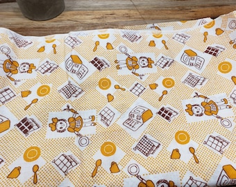 May include: White cotton tea towel with a yellow and brown pattern. The pattern features a repeating design of a girl holding a spoon, a stove, and a checkered pattern.