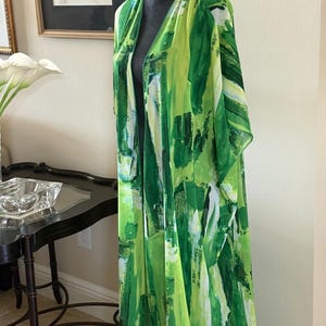Könnte beinhalten: Langes Kimono-Kleidungsstück in Grün- und Weißtönen, ausgestellt auf einer schwarzen Schaufensterpuppe. Der Stoff weist ein kühnes, abstraktes Pinselstrich-Design auf. Das Kleidungsstück hat einen V-Ausschnitt und eine offene Vorderseite.