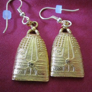 Könnte beinhalten: Ein Paar goldfarbene Ohrringe mit einem Glockendesign und filigranen Details. Die Glocken haben eine strukturierte Oberfläche und hängen an einem einfachen Haken.