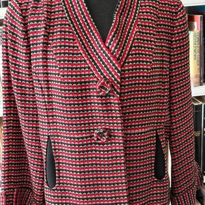 May include: A vintage red, black, and white patterned jacket with a notched collar and two buttons. The jacket has black trim and two front pockets. The sleeves are three-quarter length. The jacket is displayed on a mannequin.