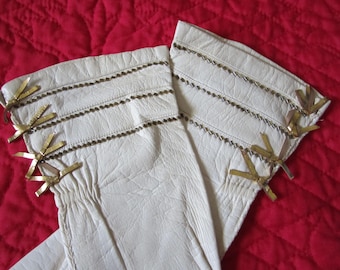 May include: A pair of white leather gloves with gold trim and bows. The gloves are long and have a decorative design.
