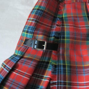 Può includere: Un kilt in tartan rosso, blu, verde e giallo con una cinghia in pelle nera e una fibbia.
