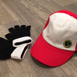 Könnte beinhalten: Eine rot-weiße Baseballkappe mit einem grünen Logo auf der Vorderseite. Die Kappe wird mit zwei schwarzen Fingerlosen Handschuhen mit weißen Bündchen geliefert.