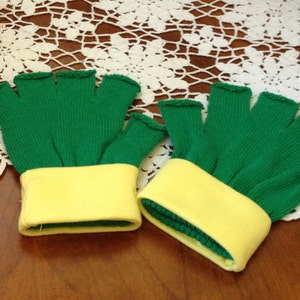 May include: A pair of fingerless gloves featuring a vibrant green knit fabric for the hand section and a contrasting solid yellow cuff at the wrist. The gloves have open finger holes with finished edges, providing a clear view of the green material.