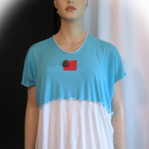 May include: A turquoise and white tunic top with a red square on the chest. The top has a ruffled hem and is worn with white capri pants.