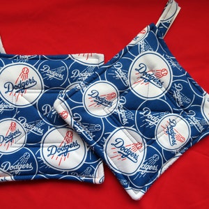 May include: Two blue and white pot holders with the Los Angeles Dodgers logo repeated on the fabric. The pot holders have a loop for hanging.