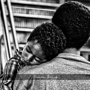 May include: A black and white photo of a young child sleeping on the shoulder of an adult. The child is wearing a plaid shirt and the adult is wearing a grey shirt.