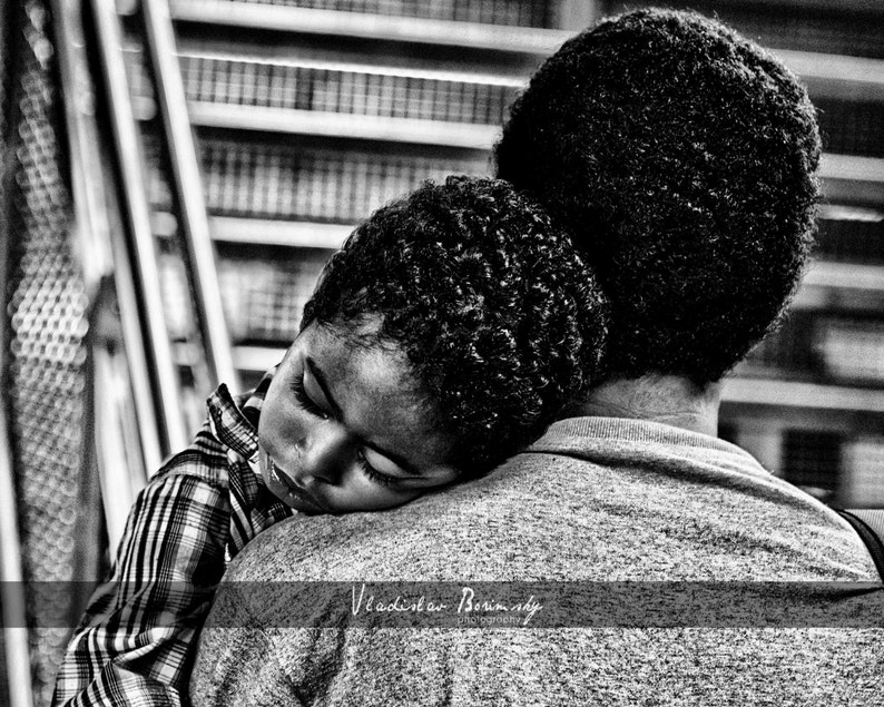 May include: A black and white photo of a young child sleeping on the shoulder of an adult. The child is wearing a plaid shirt and the adult is wearing a grey shirt.