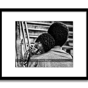 May include: A black and white photograph of a man holding a young child who is sleeping on his shoulder. The child's head is resting on the man's shoulder, and the man's arm is wrapped around the child's back. The man is looking straight ahead, and the child's face is turned to the side. The photo is taken from a low angle, and the background is blurred.