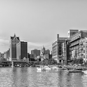 Könnte beinhalten: Ein Schwarzweißfoto einer Skyline mit Gebäuden entlang eines Flusses. Im Fluss liegen Boote vor Anker.