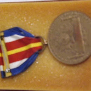 May include: A red, white, and blue ribbon medal with a gold pin and a bronze coin with a design on it. The medal and coin are displayed in a brown velvet box.