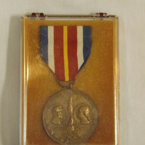 May include: A bronze medal with a ribbon in a clear plastic case. The medal features a design of two figures with a torch and the words "Veterans of Foreign Wars of the United States".
