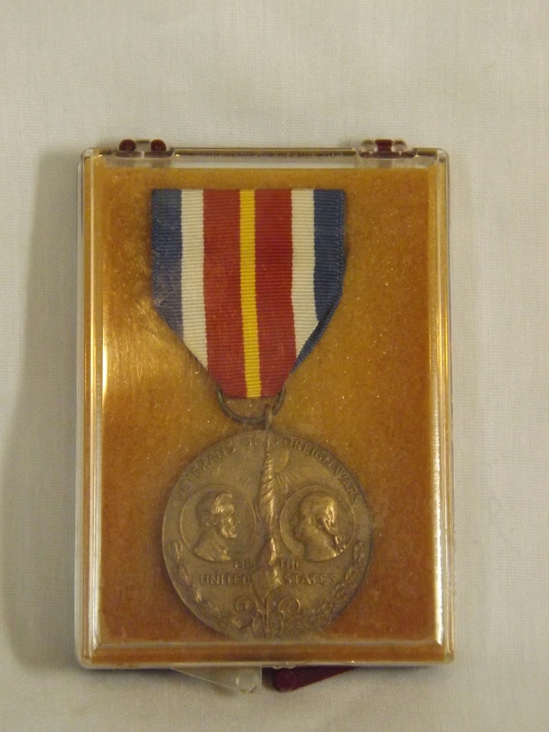 May include: A bronze medal with a ribbon in a clear plastic case. The medal features a design of two figures with a torch and the words "Veterans of Foreign Wars of the United States".