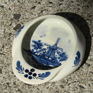 May include: A white ceramic dish with a blue and white Delft design of a windmill and a landscape. The dish has a rounded shape and a raised rim.
