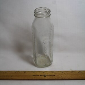 May include: A clear glass bottle with a textured surface and a label that says "Karo" on it. The bottle is empty and has a round opening at the top.