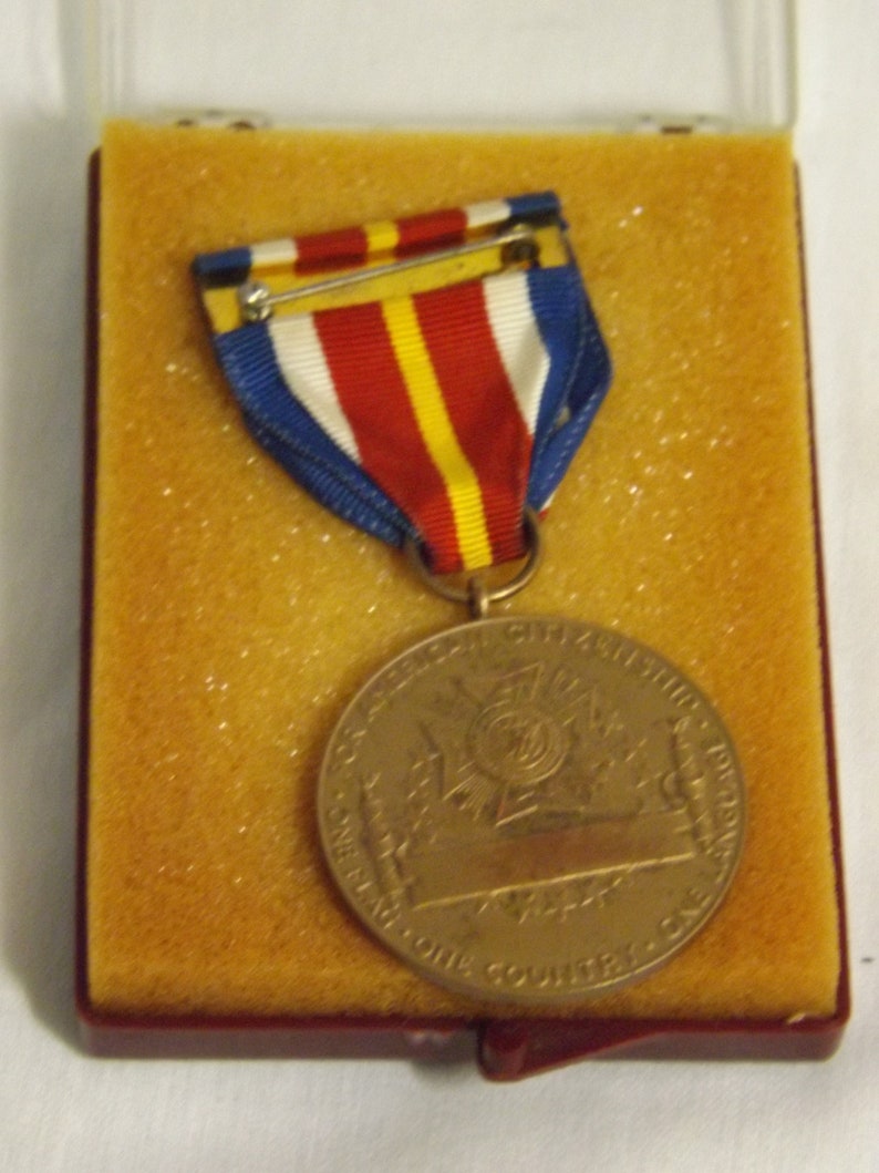 May include: A bronze medal with a red, white, and blue ribbon. The medal features a design of a ship with the text "SERVICE ABOVE SELF" and "ONE NATION ONE COUNTRY ONE CAUSE".
