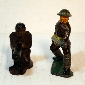 May include: Two vintage toy soldiers, one kneeling with a machine gun and the other standing with a rocket launcher. Both are painted in brown, black, and green.
