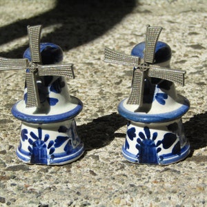 May include: Two blue and white ceramic windmills with silver metal blades. The windmills are decorative and have a traditional Dutch design.