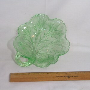 May include: A green glass leaf-shaped dish with a handle. The dish is decorated with a raised leaf pattern.