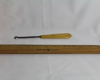 May include: A yellow plastic shoe horn with a metal hook. The shoe horn is about 6 inches long and is shown next to a wooden ruler.