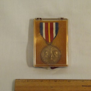 May include: A bronze medal with two profiles on the front, a red, white, and blue ribbon, and a brown velvet display case.