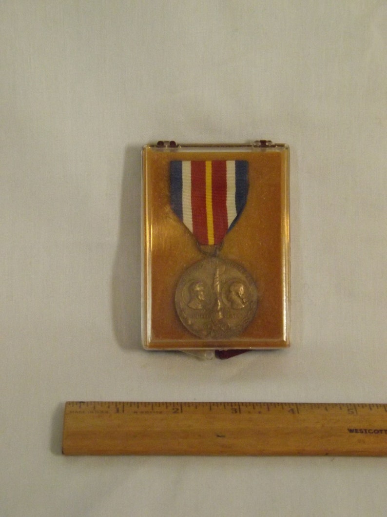 May include: A bronze medal with two profiles on the front, a red, white, and blue ribbon, and a brown velvet display case.