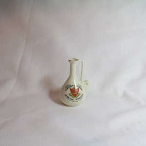 Pode incluir: Um pequeno jarro de cerâmica branca com uma alça. O jarro tem uma borda dourada e um brasão vermelho e branco com o texto "The Worshipful Company of Tallow Chandlers" e "Founded 1463 Incorporated 1505".