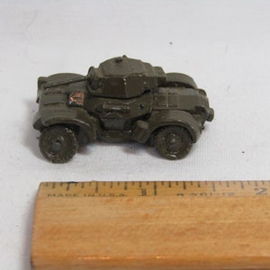 May include: A green toy armored car with a rotating turret and wheels. The car is about 2 inches long.