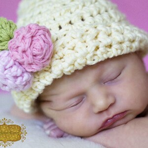 May include: A sleeping baby wearing a crocheted hat with pink and green flower embellishments.