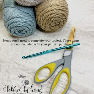 May include: Three balls of yarn in beige, light blue, and gray, a pair of yellow-handled scissors, and a turquoise crochet hook. The text "Pattern by Babies by Hand Props and Patterns" is at the bottom of the image.