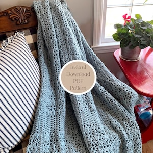 Puede incluir: Una manta de crochet azul claro drapeada sobre una silla con un patrón de cuadros blanco y negro. La manta tiene un delicado patrón de punto abierto. Un letrero dice "Descarga instantánea del patrón PDF".