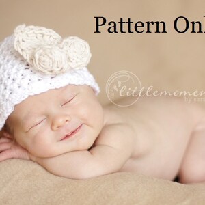 May include: A white crocheted baby hat with a flower design. The hat is on a sleeping baby. The text "Pattern Only" is above the baby and the text "littlemoments by sarah" is below the baby.