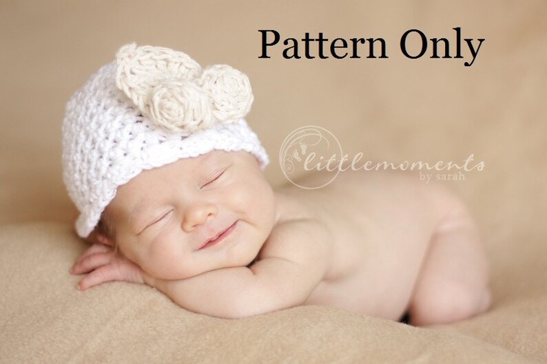 May include: A white crocheted baby hat with a flower design. The hat is on a sleeping baby. The text "Pattern Only" is above the baby and the text "littlemoments by sarah" is below the baby.