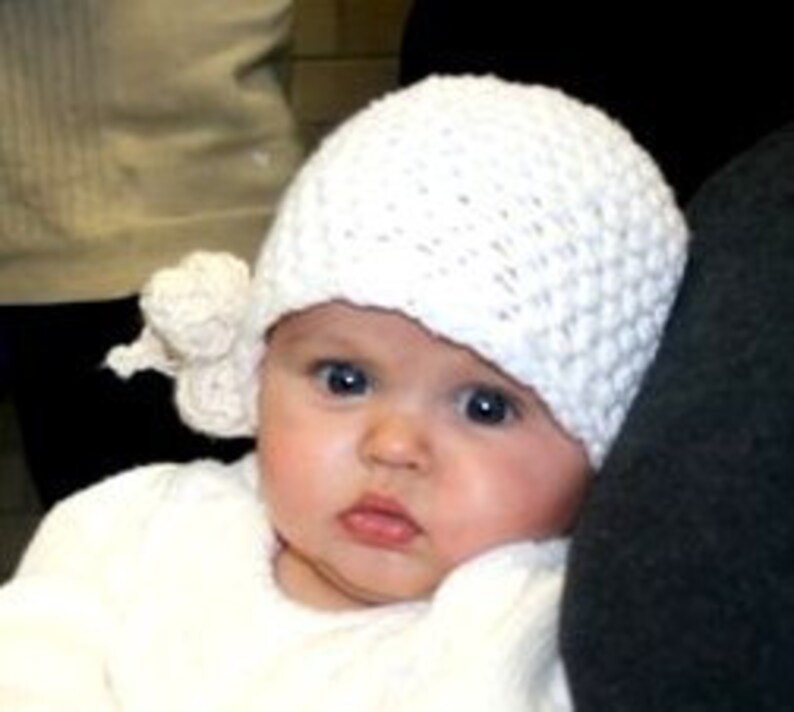 May include: A white crocheted baby hat with a white crocheted flower on the side.