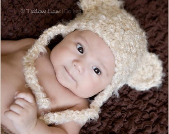 May include: A baby wearing a cream crocheted bear hat with floppy ears. The hat has a long strap that ties under the chin. The baby is lying on a brown textured blanket. © Teddanne Lucius | Do Not Copy