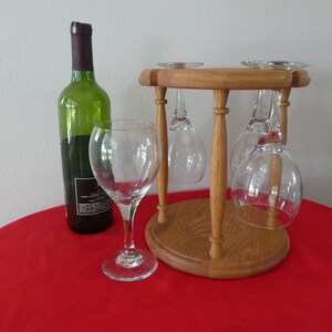 May include: A wooden wine glass holder with four glasses hanging upside down. A bottle of wine is on a red tablecloth.
