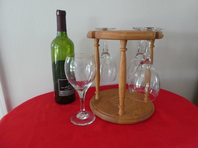 May include: A wooden wine glass holder with four glasses hanging upside down. A bottle of wine is on a red tablecloth.